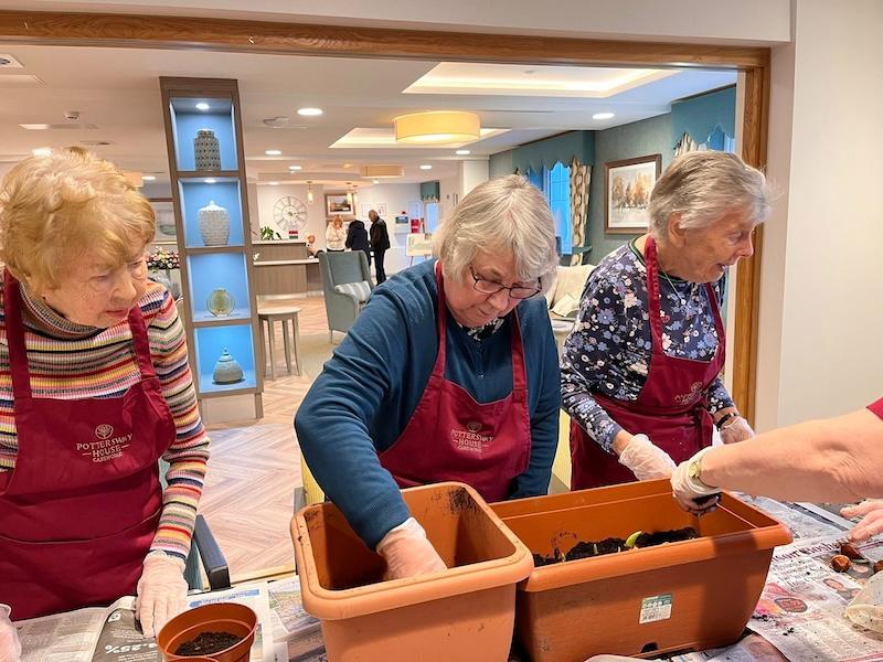 3 female residents stood up planting flowers in pots