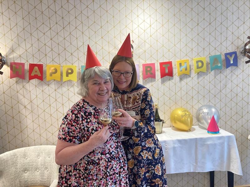 elderly resident and our home manager stood together in floral dresses holding up glasses of wine smiling