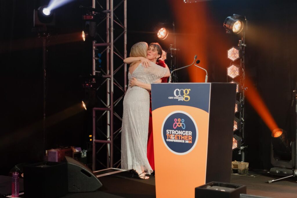 two ladies hugging on a stage for a celebration