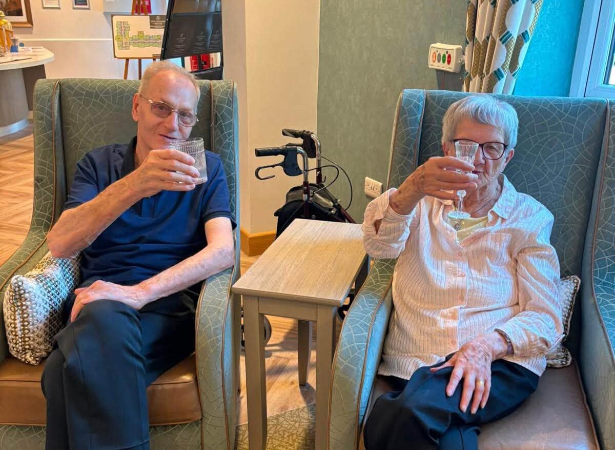 older adults sat down holding up glasses