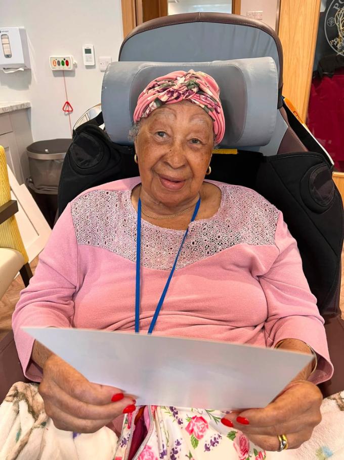 older lady with a headscarf sat in a chair smiling