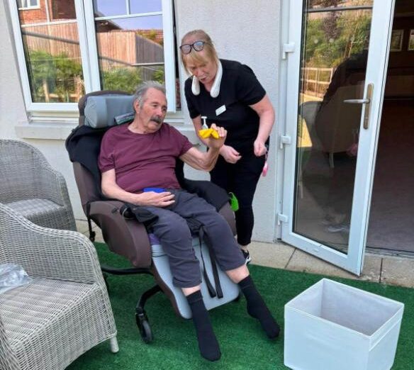 older man in a wheelchair outside with staff